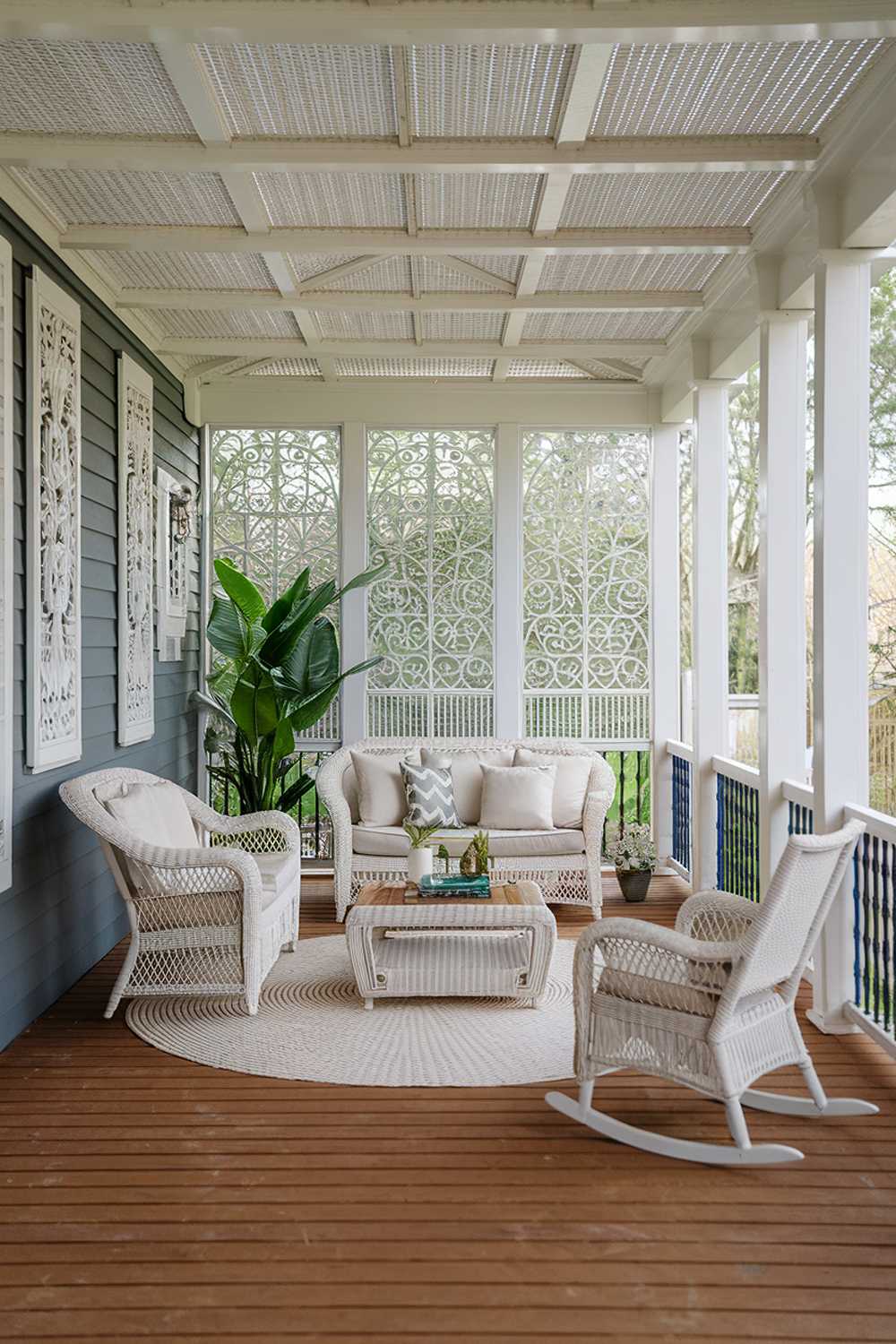 White wicker furniture and green plants create bright, airy back porch atmosphere