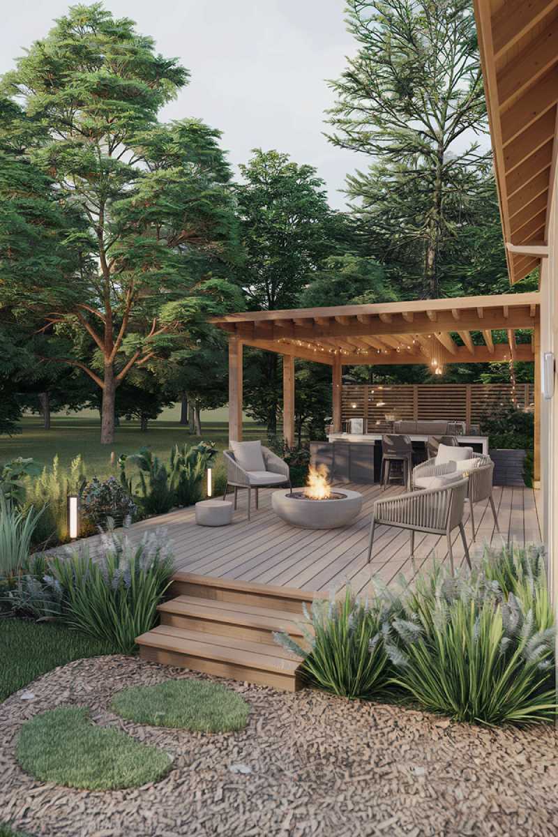 A modern patio design and decor. The patio is surrounded by lush greenery, with a few trees and plants. There's a wooden deck leading to the patio. The patio has a fire pit, a few chairs, and a table. There's a wooden structure with a roof in the background. The ground is covered with gravel. The overall ambiance is serene and inviting.