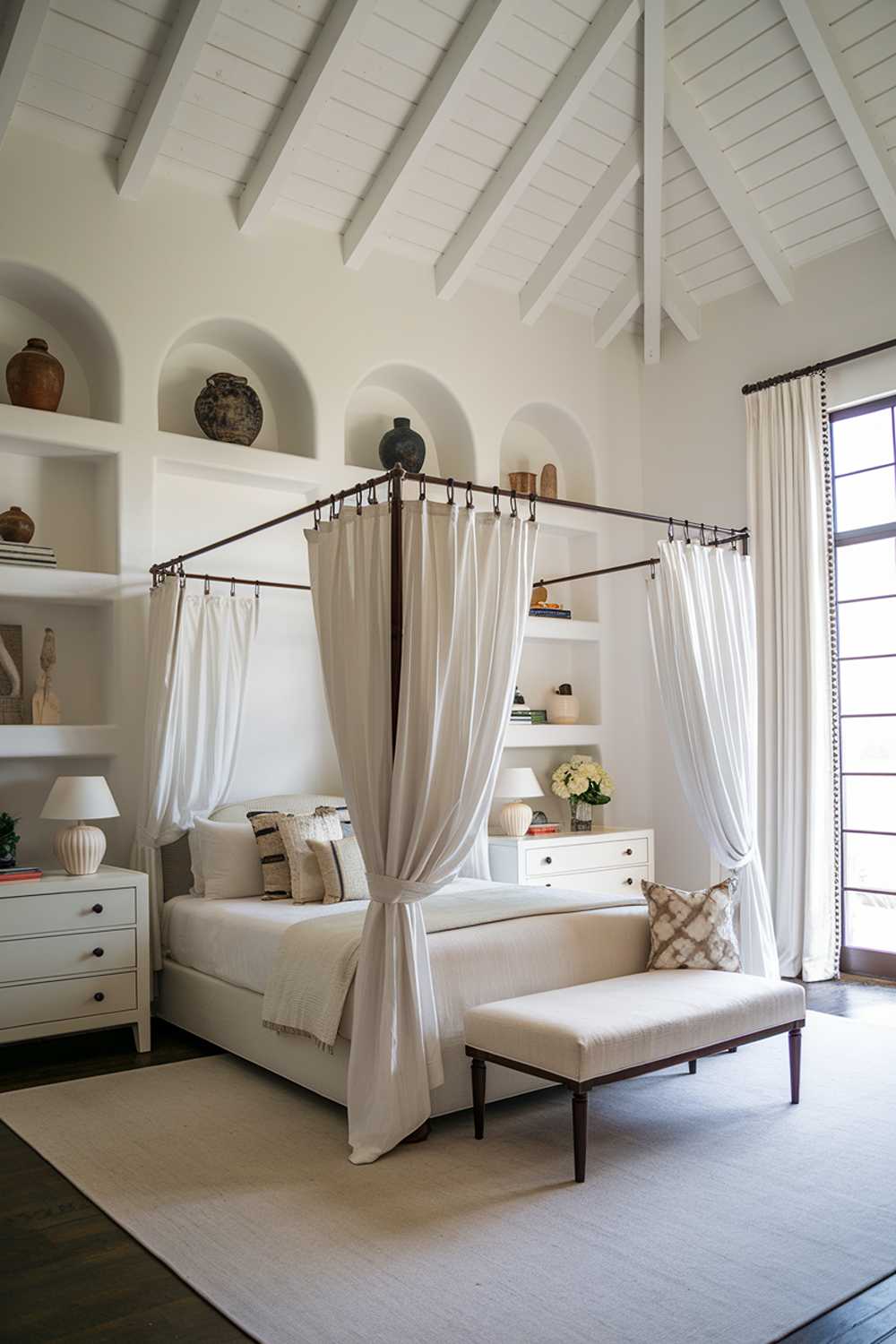 An all white bedroom with a high ceiling. The room has a canopy bed with white curtains. There's a white dresser and a nightstand next to the bed. The floor is covered with a white rug. The walls have white shelves with decorative items. The room has a large window with white curtains.